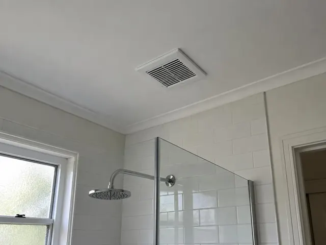 Bathroom ceiling exhaust fan above tiled shower area with glass screen in a light tiled bathroom in Chatswood